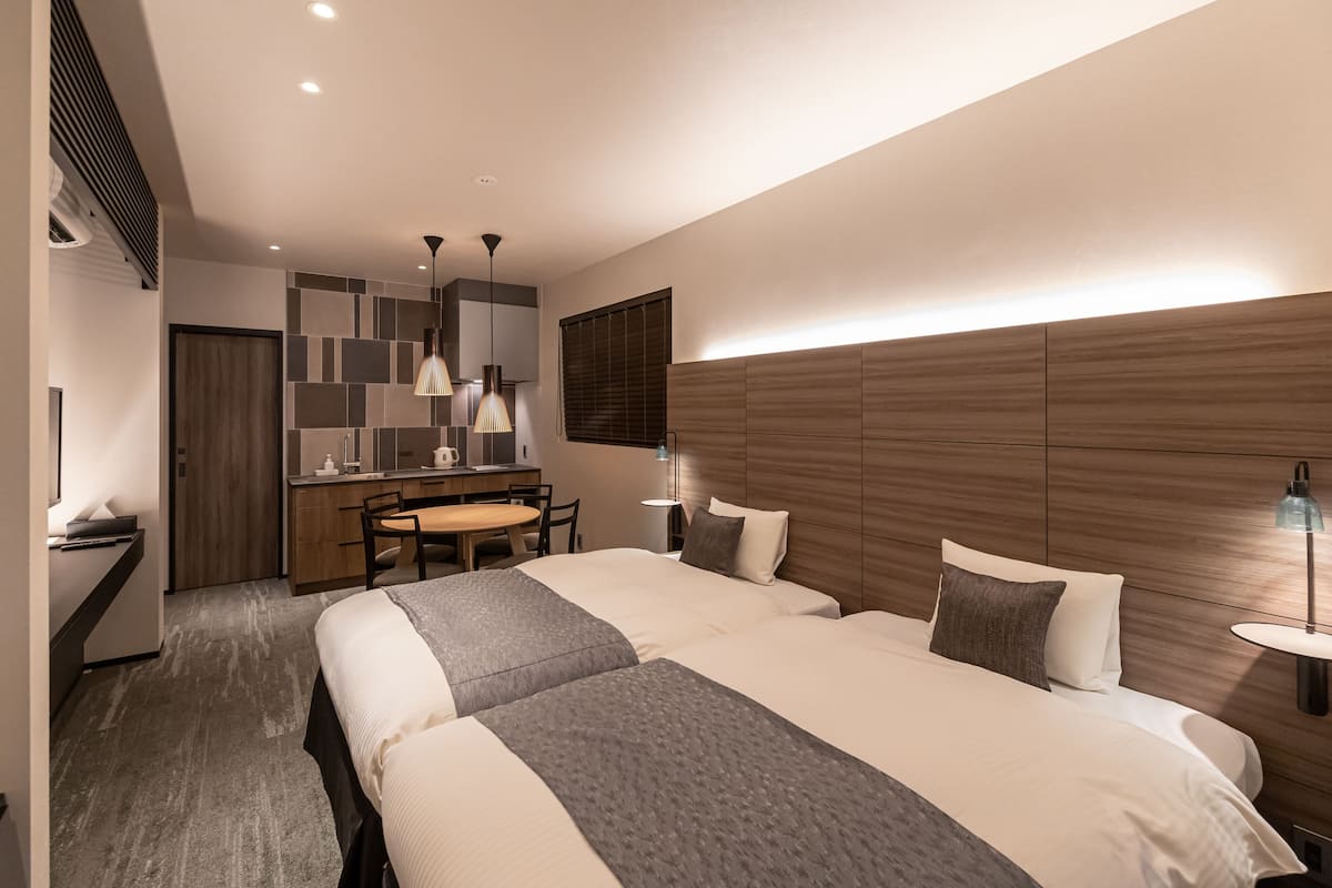 Une chambre d’hôtel moderne avec deux lits, une tête de lit en bois, un bureau avec une chaise et un coin repas.