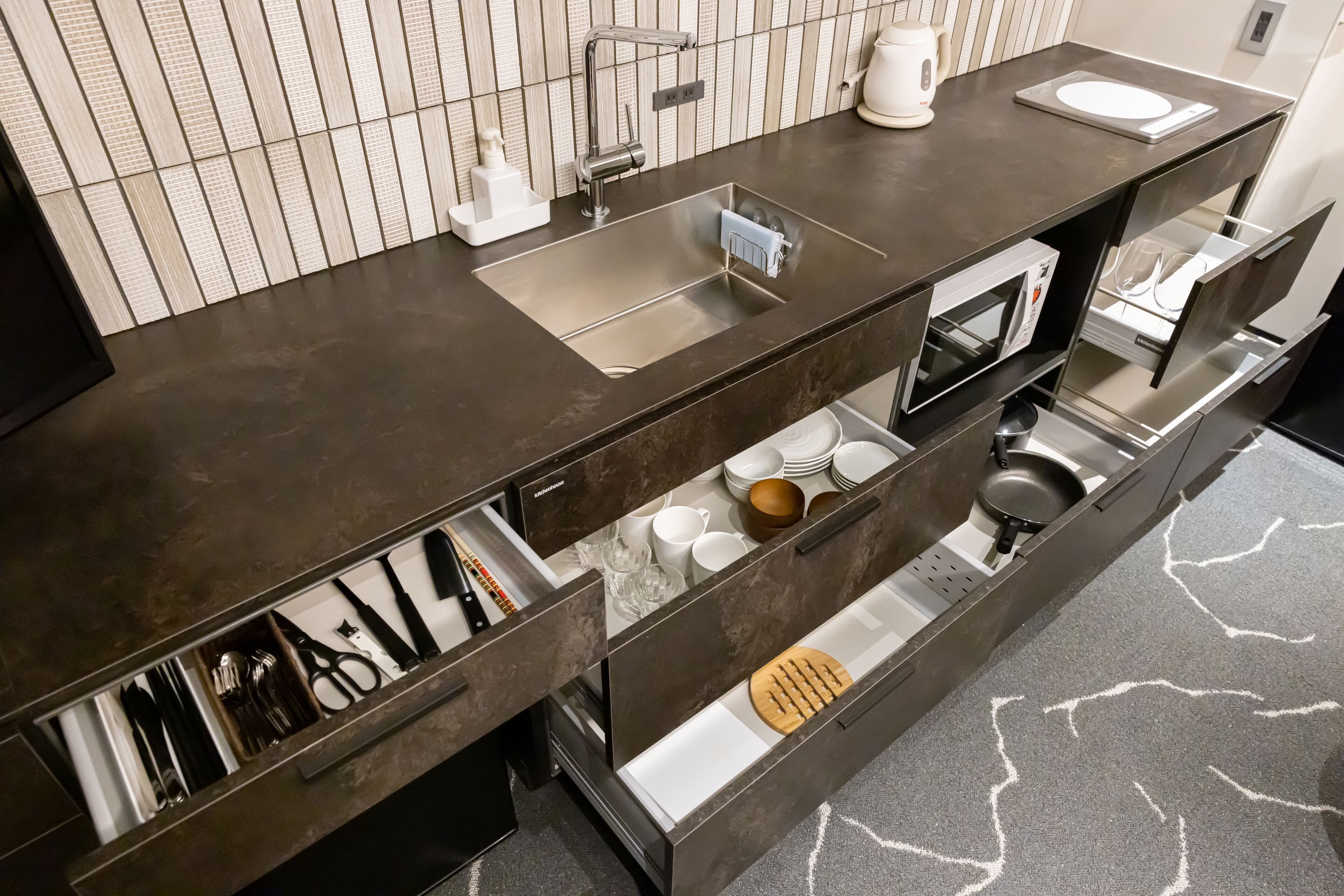 A modern kitchen with a dark countertop, stainless steel sink, and built-in appliances.