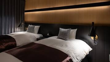 Habitación de hotel con dos camas, cabecera de madera oscura, iluminación moderna y una mesita de noche con lámpara.