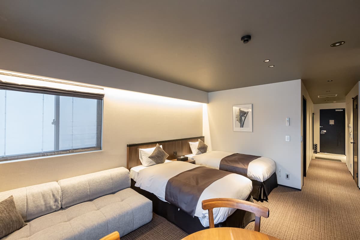 Une chambre d’hôtel avec deux lits, un canapé, un fauteuil et une grande fenêtre.