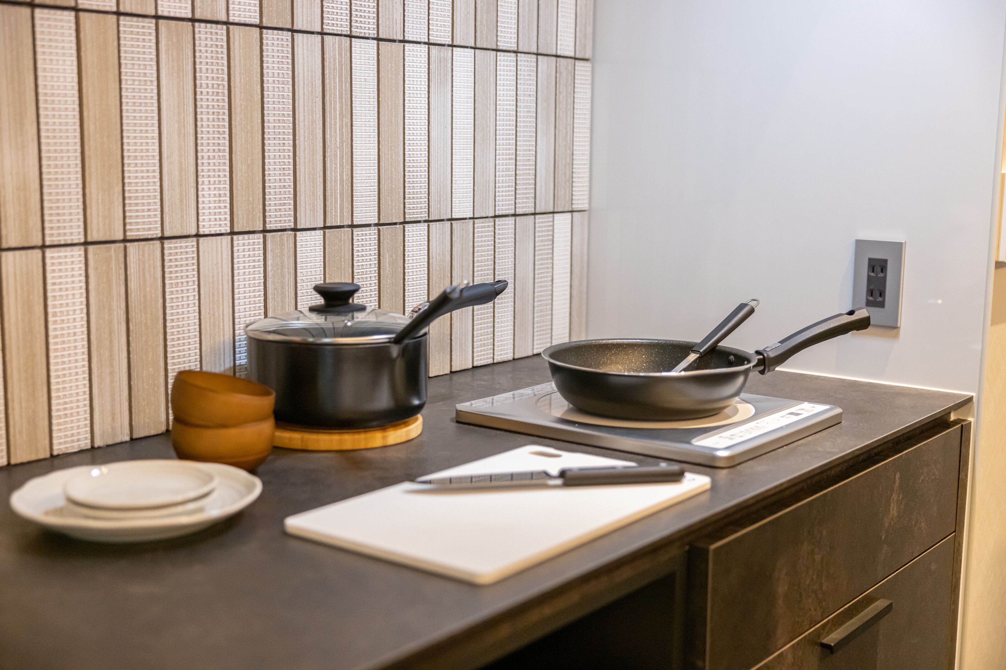 A kitchen counter with a frying pan, a pot, a cutting board, and a knife.