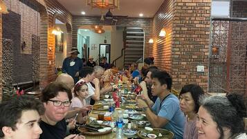 A group of people dining at a long table in a restaurant with brick walls and a ceiling fan.