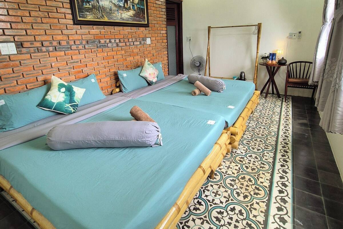 A room with a brick wall, a painting, a bed with blue sheets, and a patterned floor.