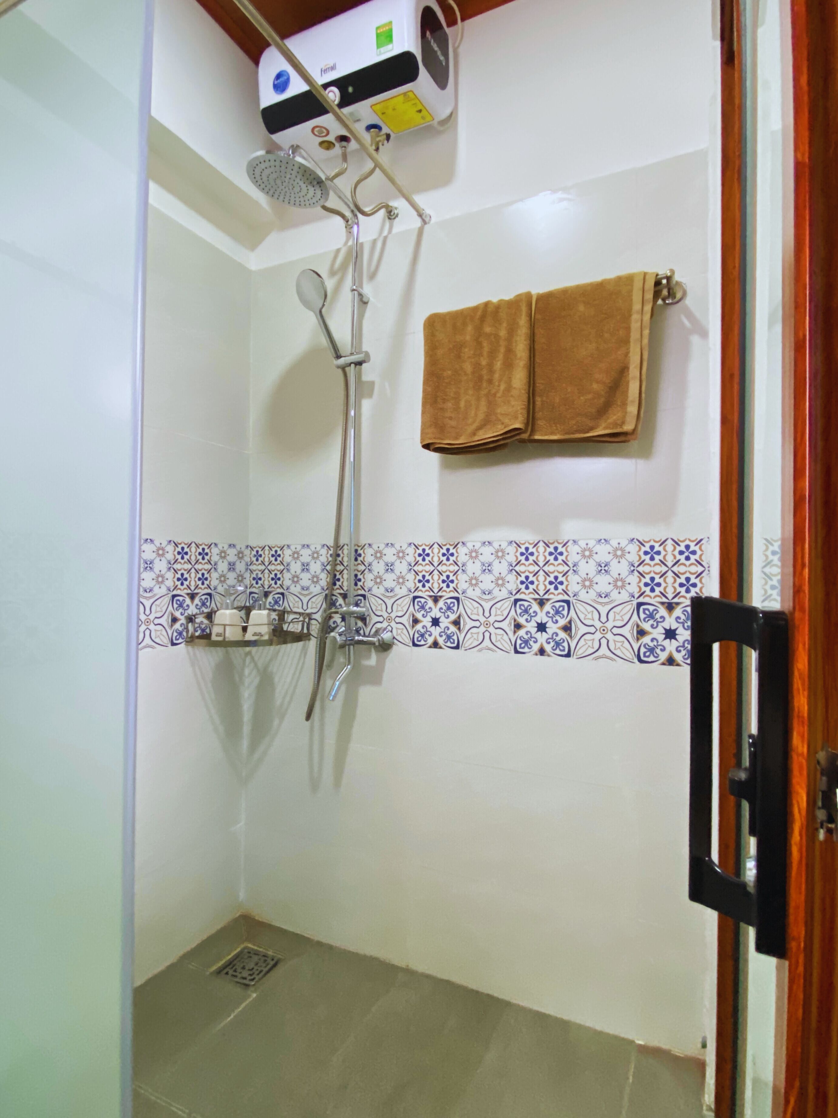 A shower with a handheld showerhead and a wall-mounted faucet, a towel rack with a brown towel, and a tiled shower area.
