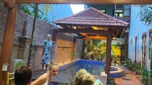 Ein überdachter Außenbereich mit Essbereich, Pool, einer Holz-Pergola und gefliestem Boden.