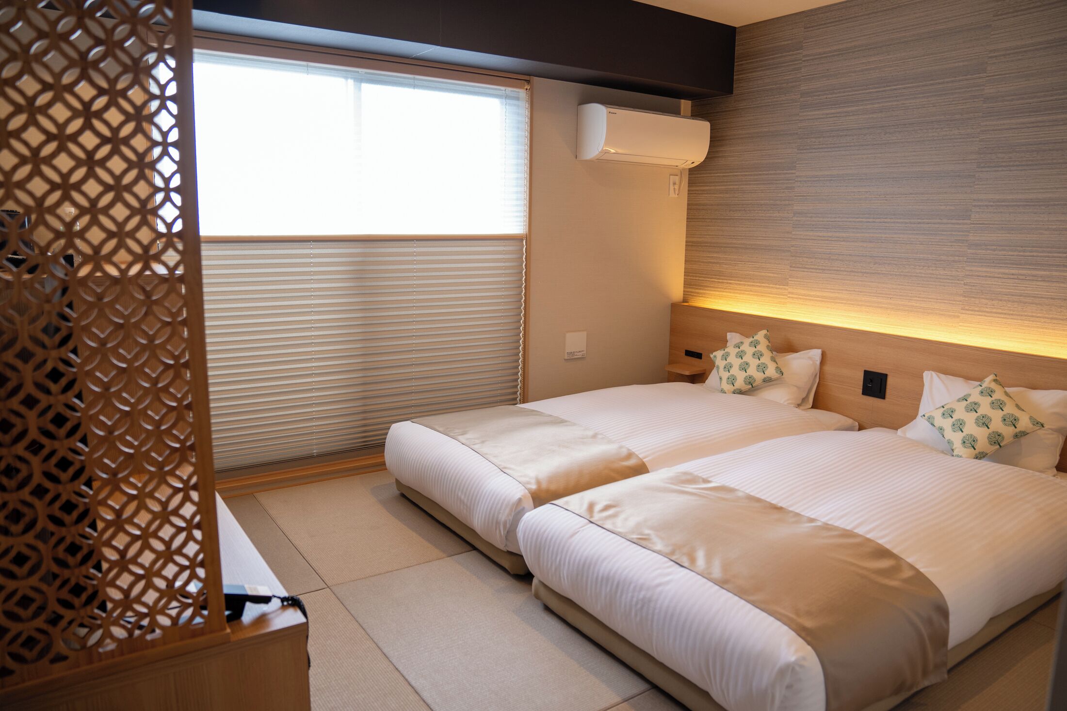 Ein Hotelzimmer mit zwei Betten, einem Fenster mit Jalousien, einer Klimaanlage und einer Holzwand.