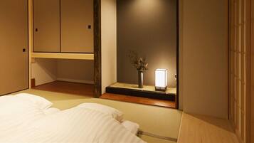 Habitación de hotel con cama, mesita de noche con lámpara, pequeño florero con flores y armario con puerta corredera.