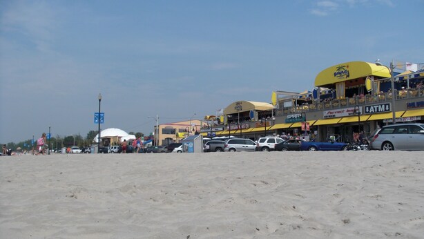 A beachside area with a row of shops and a beach in the foreground. - Cozy 2BR Cottage • Walk to Beach 1 • Free Parking & WiFi (Wasaga Beach)