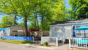 A row of mobile homes with white railings, a picnic table, and a small tree in the foreground. - Cozy 2BR Cottage • Walk to Beach 1 • Free Parking & WiFi (Wasaga Beach)
