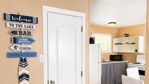 A room with a white door, a kitchen area with a microwave and stove, and a bar sign on the wall. - Cozy 2BR Cottage • Walk to Beach 1 • Free Parking & WiFi (Wasaga Beach)
