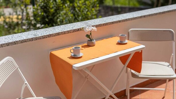 A small outdoor table with two chairs, a potted plant, and two cups.