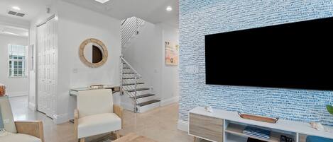 A modern living room with a staircase, a flat-screen TV, and a patterned wall.