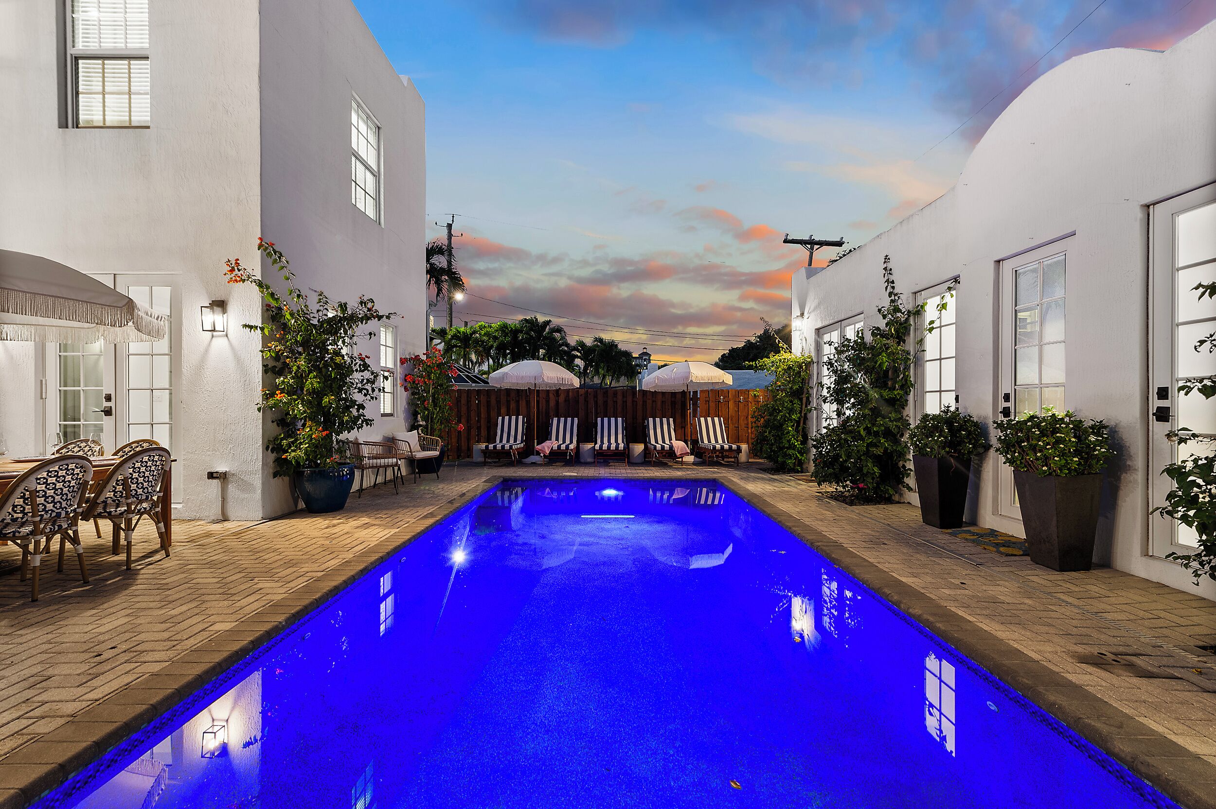 Una piscina de color azul, rodeada de paredes blancas, mobiliario exterior y plantas en macetas.