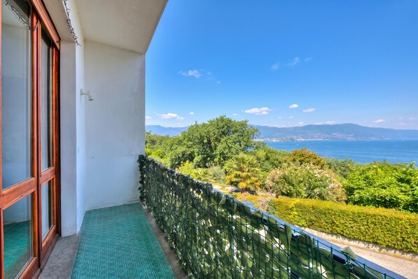 Een balkon met uitzicht op zee en bergen, een vloer met een groen patroon en een metalen reling.
