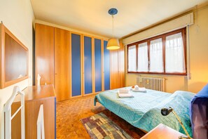Een slaapkamer met een bed, bureau, stoel, raam met gordijnen en een radiator.