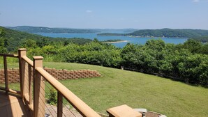 Una terraza de madera con barandilla que da a un lago y colinas.