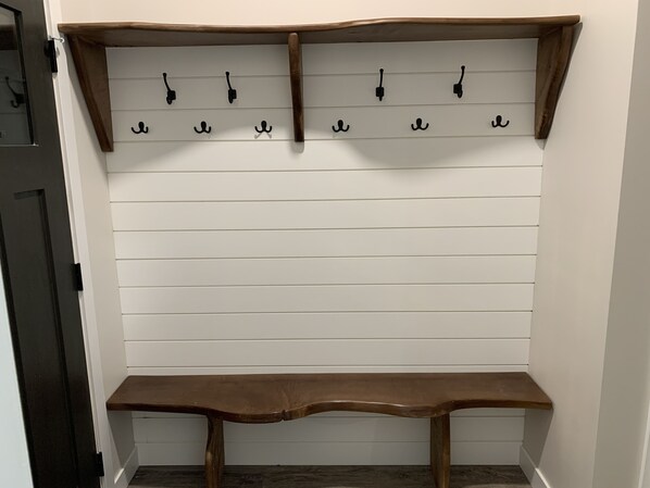 Een witte muur met horizontale panelen en een houten bankje onderaan.