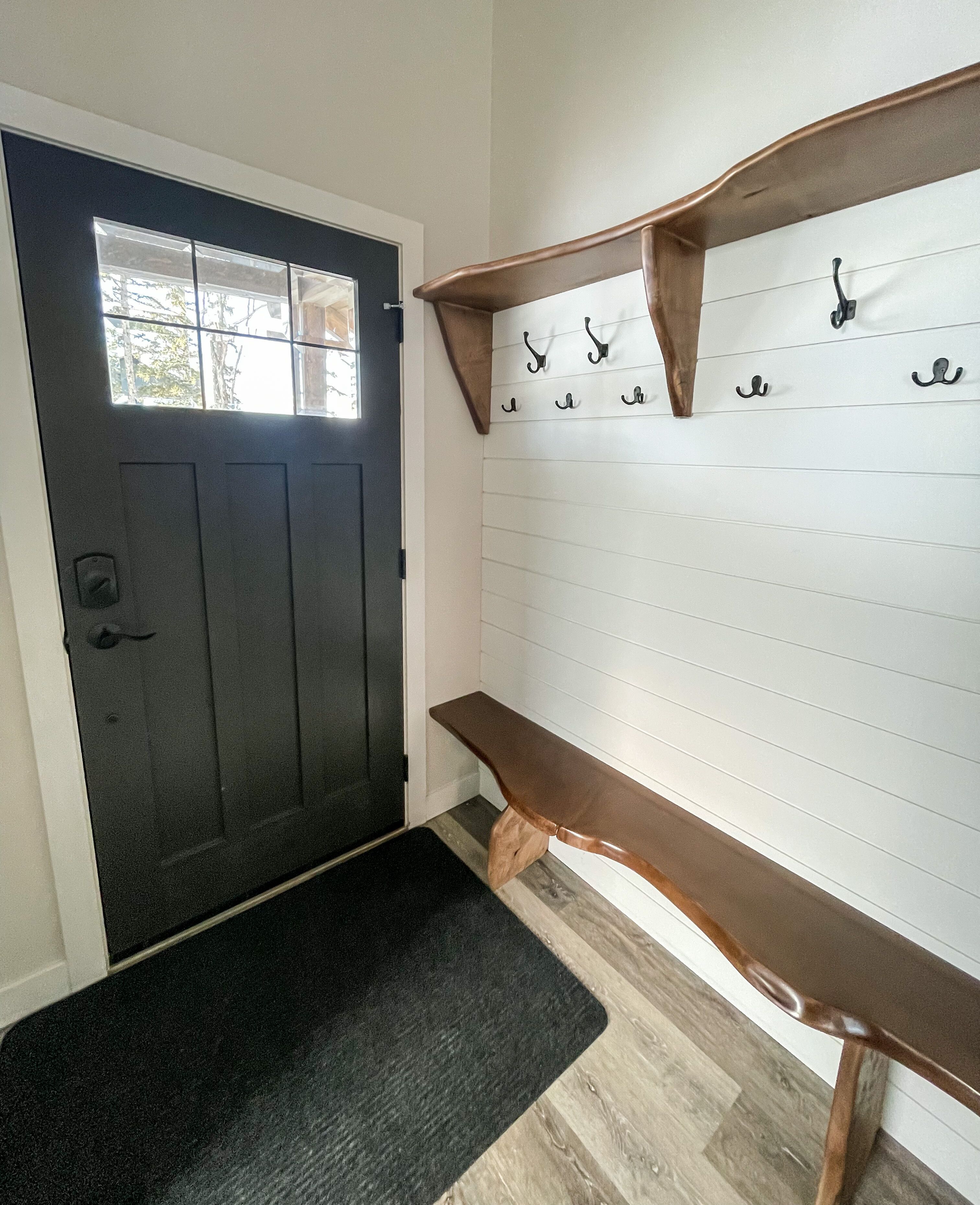 A dark wooden door with a window, a bench, and a wall-mounted coat rack with hooks.