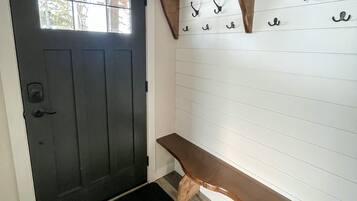 A dark wooden door with a window, a bench, and a wall-mounted coat rack with hooks.