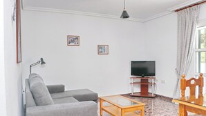 Un salon avec un canapé gris, une table basse en bois, un téléviseur posé sur un meuble et une lampe.