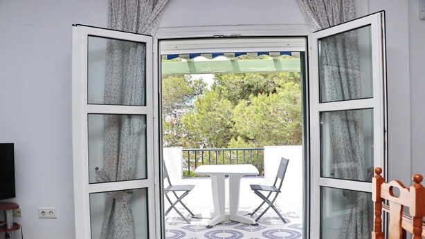 Un balcon ouvert avec une table et des chaises, une chaise en bois et un téléviseur sur le côté gauche.