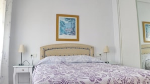 Une chambre à coucher comprenant un lit, deux tables de chevet, une commode, un tableau accroché au mur et un miroir.