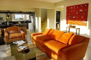 Relax in the spacious living room with a large sofa, glass coffee table, and kitchen in the background.