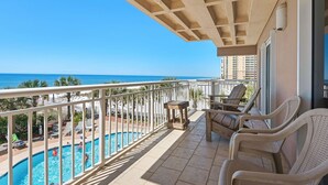 A balcony with a pool, lounge chairs, and a view of the ocean. - Destin Towers 32 (Destin)