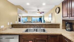 A kitchen with two stainless steel sinks, a dishwasher, wooden cabinets, a ceiling fan, and a clock on the wall. - Destin Towers 32 (Destin)