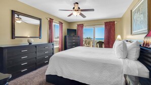 A bedroom with a bed, a ceiling fan, a dresser, a TV, and a view of the ocean. - Destin Towers 32 (Destin)
