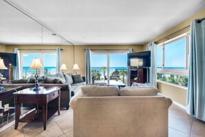 Ein geräumiges Wohnzimmer mit großem Fenster und Meerblick, einem bequemen Sofa, einem Couchtisch und einem Flachbildfernseher.