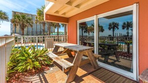 A wooden table and bench on a balcony with a pool view.