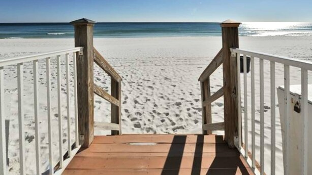 A wooden boardwalk leading to a sandy beach with a clear blue sky.