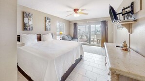 A hotel room with a bed, a desk, a ceiling fan, a TV, and a balcony with a view.