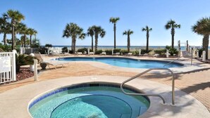 A swimming pool with a small hot tub, surrounded by palm trees and a view of the ocean.