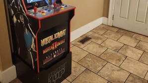 Ein Mortal Kombat Arcade-Spiel in einer Ecke, mit einer beigefarbenen Wand und einer weißen Tür.