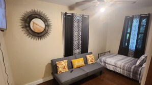 Ein Zimmer mit grauem Sofa, einem gemusterten Vorhang, einem Deckenventilator und einem Fenster mit Aussicht.