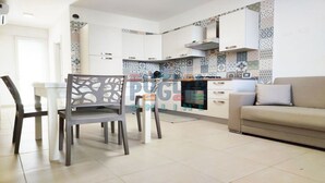 Une cuisine moderne avec des armoires blanches et des carreaux de crédence à motifs. On y trouve un coin repas avec une table et des chaises, ainsi qu’un canapé dans le salon.