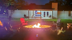 Zona exterior amb seients, un foc de llar, cadirees i un edifici amb una bandera al fons.