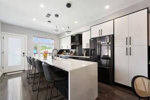 Een moderne keuken met een groot eiland, roestvrijstalen apparatuur en uitzicht op de buitenruimte.