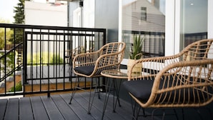 En balkon med fletstole og et lille bord, med udsigt over et boligområde.