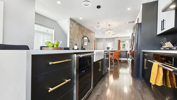 A modern kitchen with black cabinets, gold handles, and a wooden floor. - ★ HostWise Stays ★ Rooftop Deck & Fire Pit Haven | Theater & Balcony (Pittsburgh)