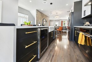 A modern kitchen with black cabinets, gold handles, and a wooden floor. - ★ HostWise Stays ★ Rooftop Deck & Fire Pit Haven | Theater & Balcony (Pittsburgh)