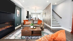 A modern living room with a fireplace, a sofa set, a coffee table, and a staircase. - ★ HostWise Stays ★ Rooftop Deck & Fire Pit Haven | Theater & Balcony (Pittsburgh)