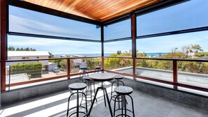 Un balcon moderne avec un plafond en bois, de grandes fenêtres et une vue sur la mer.