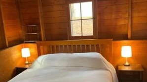 A wooden cabin room with a bed, two bedside lamps, and a window. - Lake St Catherine Cabin For Two with deck and lake access (Poultney)