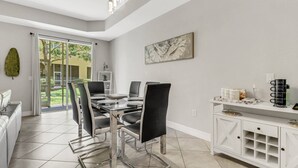 A modern dining area with a glass-top table, black upholstered chairs, and a white cabinet with storage.