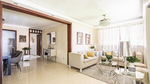 Amplia sala de estar con sofá, mesa de centro y mesa de comedor. Incluye elementos decorativos y una araña.