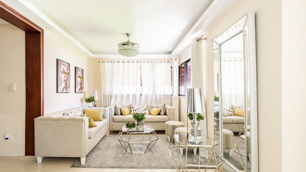 Un salón con un sofá color beige, una mesa de centro de vidrio y un espejo grande.