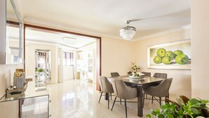 Un comedor moderno con una araña, una mesa de comedor con sillas y un cuadro de manzanas en la pared.